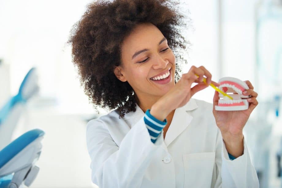 a dentist with a set of model teeth in her hand and a toothbrush