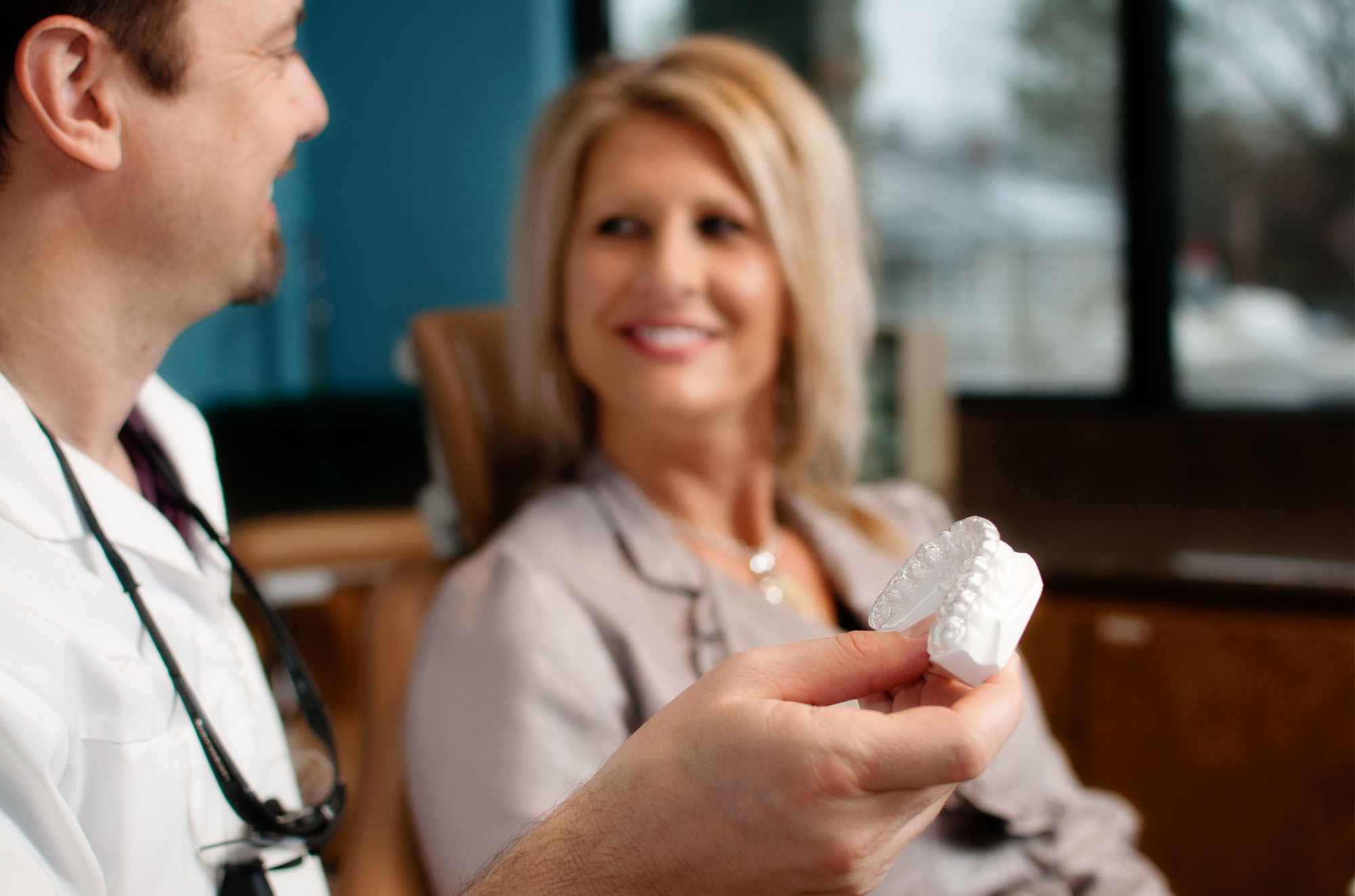 dentist holding model of teeth and talking with female patient