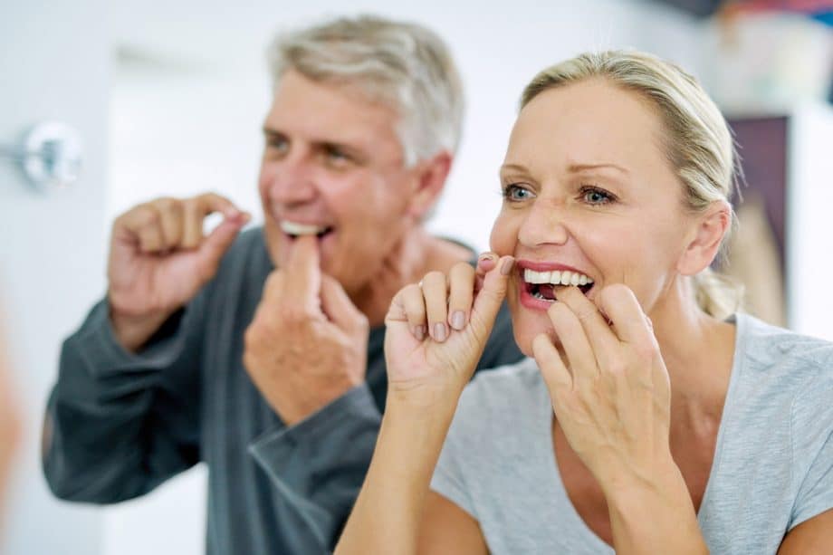 a couple flossing their teeth in the mirror