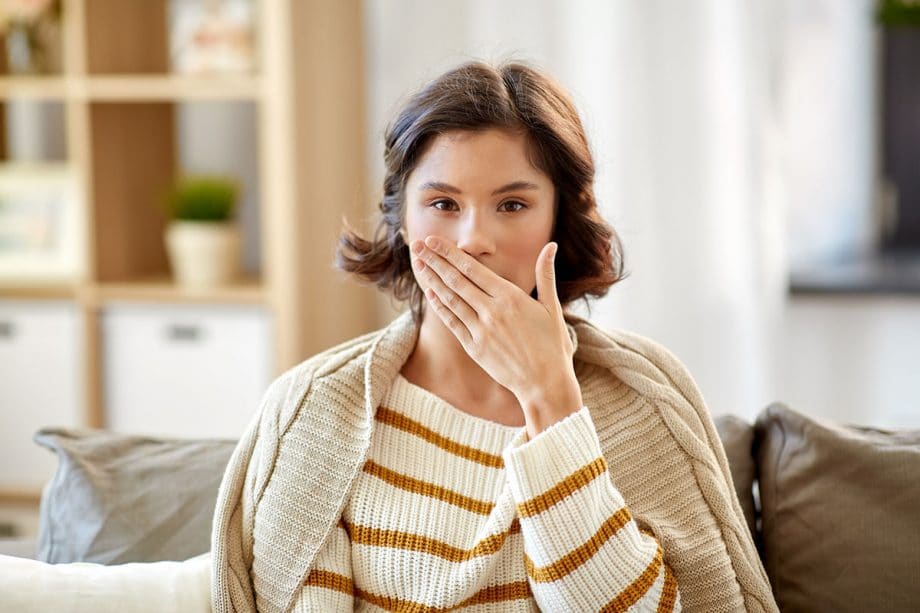 young woman sitting on couch with hand over mouth